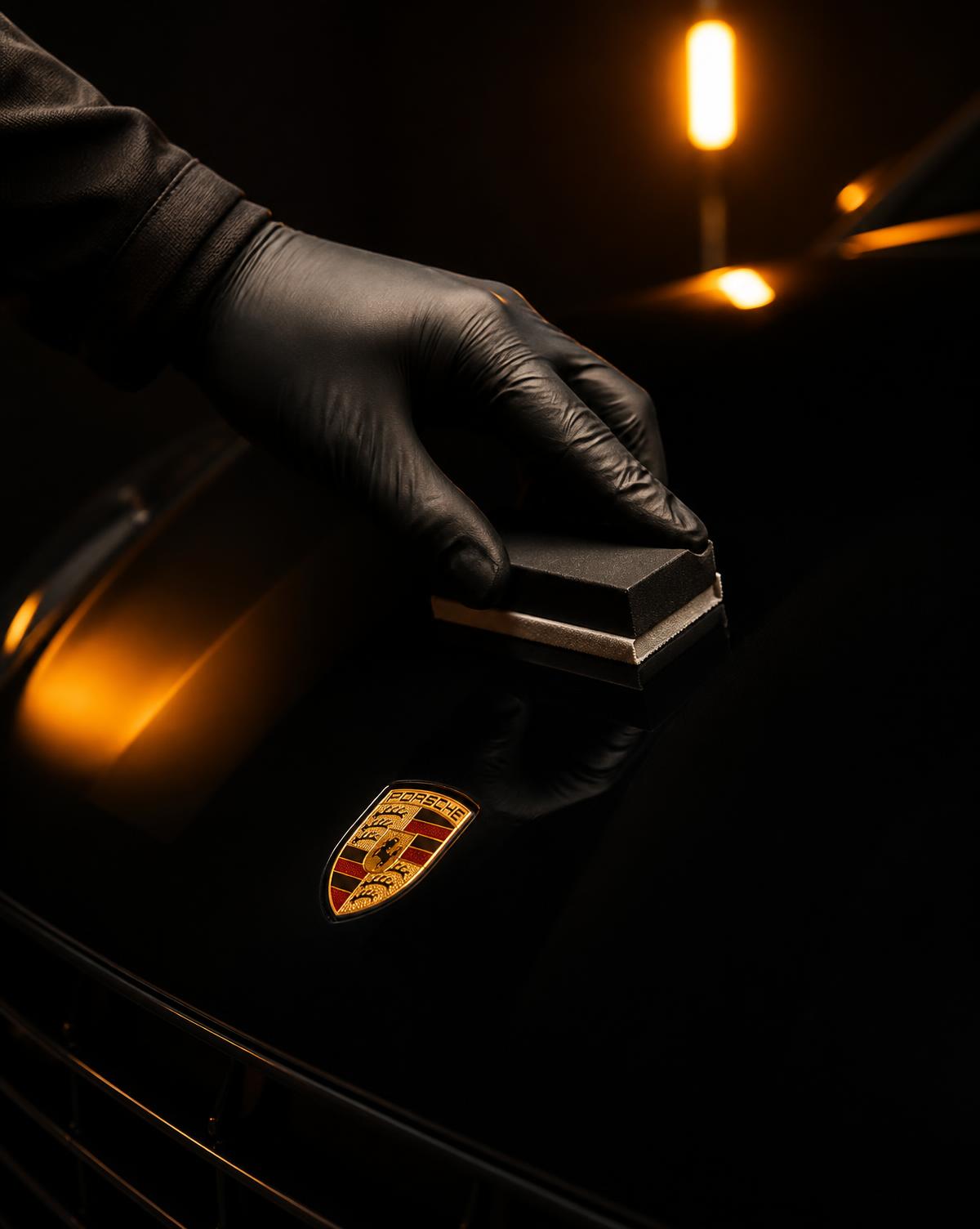 Gloved hand applying ceramic coating to a black hood with an applicator block